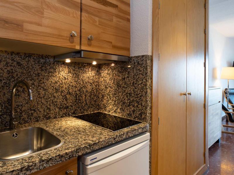 Kleine Küche mit braunem Granit, Spüle, Kochfeld und Holzschränken in hellem Licht.