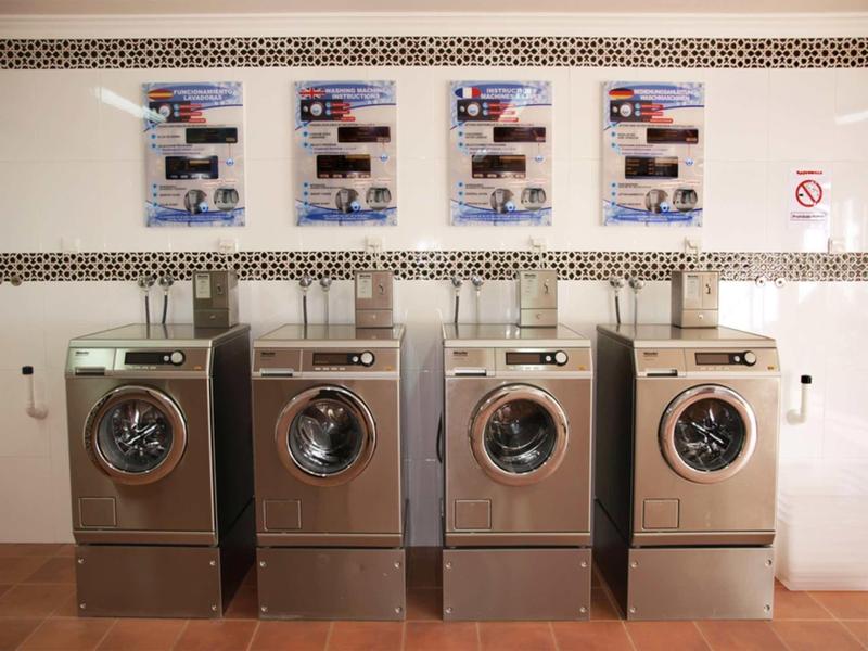 Vier silberne Waschmaschinen nebeneinander unter Anweisungen an der Wand in einem hellen Raum.