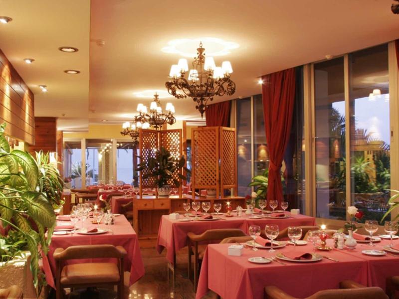 Elegantes Restaurant mit rot gedeckten Tischen, Kronleuchtern und großen Fenstern am Abend.
