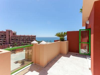 Balcony with glass railing overlooking residential buildings and sea on a clear day