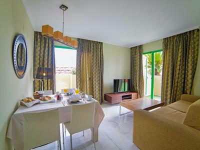 Helles Wohnzimmer mit Essbereich, Sofa, Flachbildfernseher und großen Fenstern mit Vorhängen