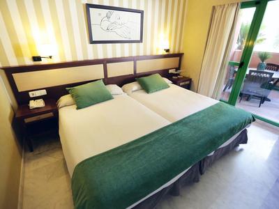 Hotelzimmer mit zwei Einzelbetten, grün-weißer Bettwäsche und Balkon mit Sitzgelegenheit.