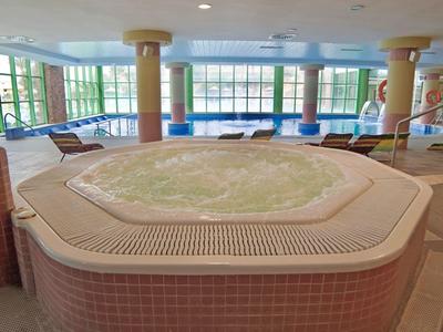 Innenbereich mit großem Whirlpool, umgeben von Säulen und großen Fenstern mit Blick auf Außenbereich.