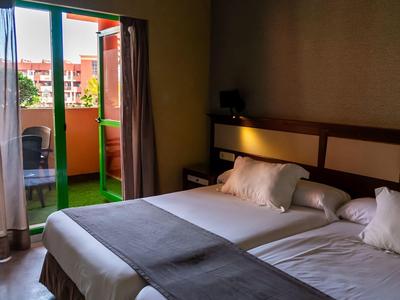 Zweibettzimmer mit offenem Balkon und Blick auf Nachbargebäude.