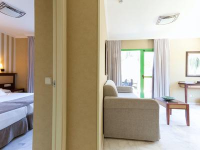 Blick in zwei nebeneinander liegende Hotelzimmer mit Betten und Sofa, getrennt durch eine Wand.