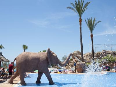 Elefant geht an einem Pool mit Palmen und Menschen vorbei.