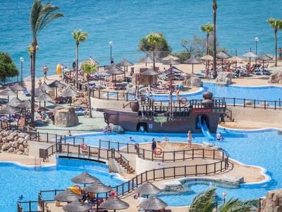 Großer Hotelpool mit Sonnenschirmen, Liegestühlen und einem Schiff als Poolbar neben dem Meer