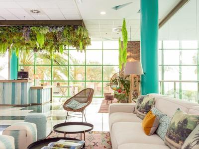 Heller Wohnraum mit großen Fenstern, weißen Sofas, grünen Vorhängen und Pflanzen als Dekor.