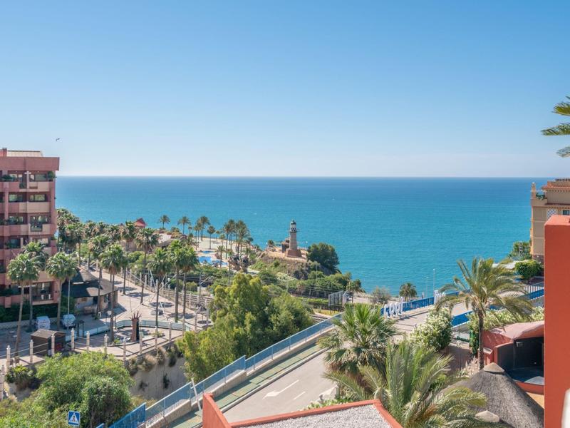 Blick auf eine Küstenstadt mit Meer, Palmen und Gebäuden bei klarem Himmel.