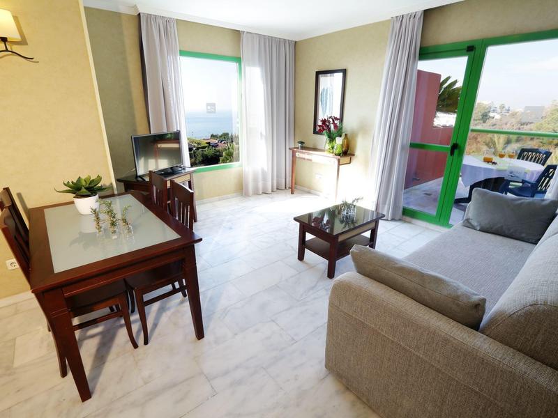 Helles Wohnzimmer mit Sofa, Esstisch und großem Balkon mit Aussicht.