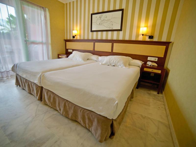 Hotelzimmer mit zwei Einzelbetten, einem Nachttisch und einem großen Fenster mit Vorhängen.