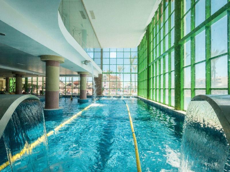 Innenansicht eines modernen Hallenbads mit Wasserfällen und großen Fenstern