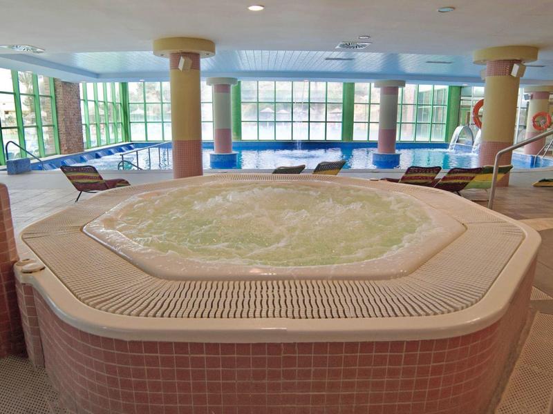 Innenbereich mit großem Whirlpool, umgeben von Säulen und großen Fenstern mit Blick auf Außenbereich.
