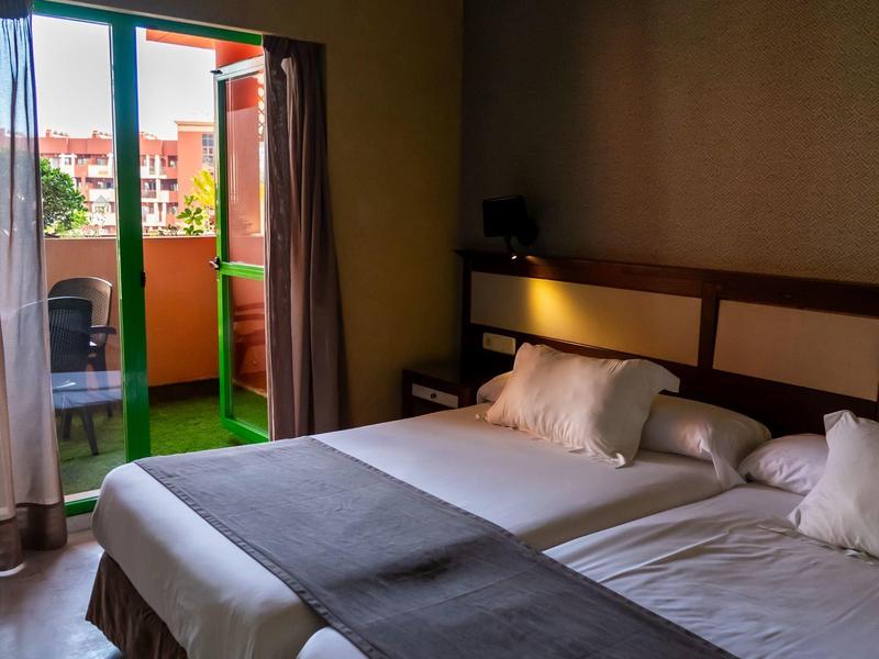 Zweibettzimmer mit offenem Balkon und Blick auf Nachbargebäude.