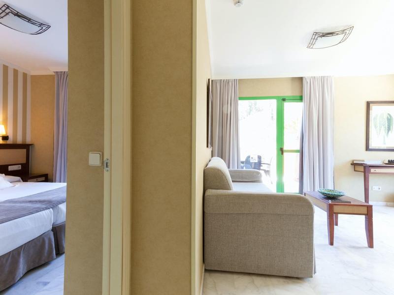 Blick in zwei nebeneinander liegende Hotelzimmer mit Betten und Sofa, getrennt durch eine Wand.