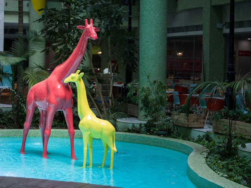 Zwei farbige Giraffenfiguren neben einem kleinen Pool in einer Hotelhalle.