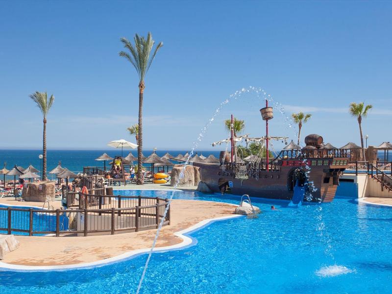 Großer Außenpool mit Palmen und Meerblick an sonnigem Tag