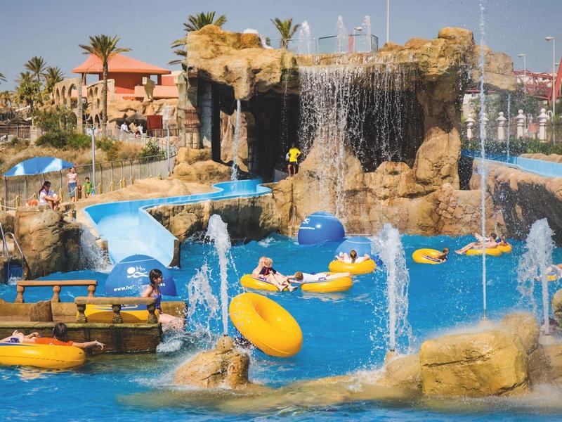 Wasserpark mit Wasserfall, Pools, Wasserrutschen und Personen auf aufblasbaren Schwimmringen