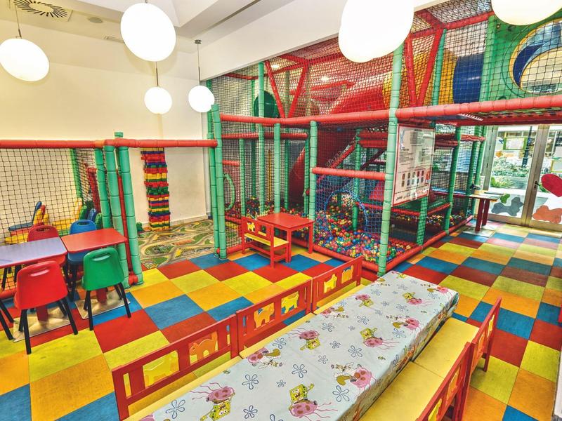 Bunter Indoor-Spielplatz mit weichen Matten, Klettergerüst und Tischen für Kinder.