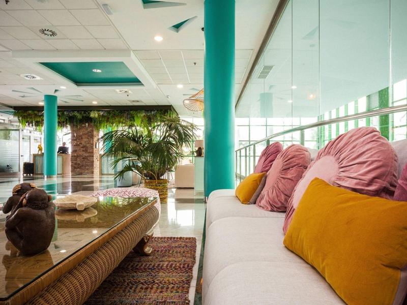 Helles, modernes Wohnzimmer mit weißen Sofa, bunten Kissen, Glaswand und Holztisch mit Dekoration.