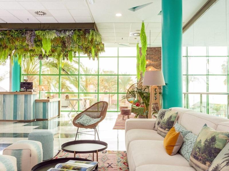 Heller Wohnraum mit großen Fenstern, weißen Sofas, grünen Vorhängen und Pflanzen als Dekor.