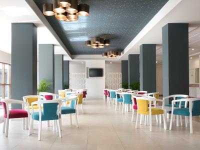 Moderner heller Speisesaal mit bunten Stühlen und großen Fenstern, viele Säulen und minimalistisches Design.