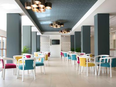 Moderner Speisesaal mit weißen Tischen, bunten Stühlen und großen Fenstern für viel Tageslicht.