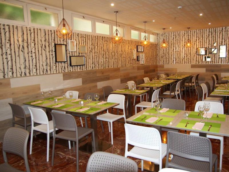 Modernes Restaurant mit Holzwänden, gemischten Stühlen und grün gedeckten Tischen.