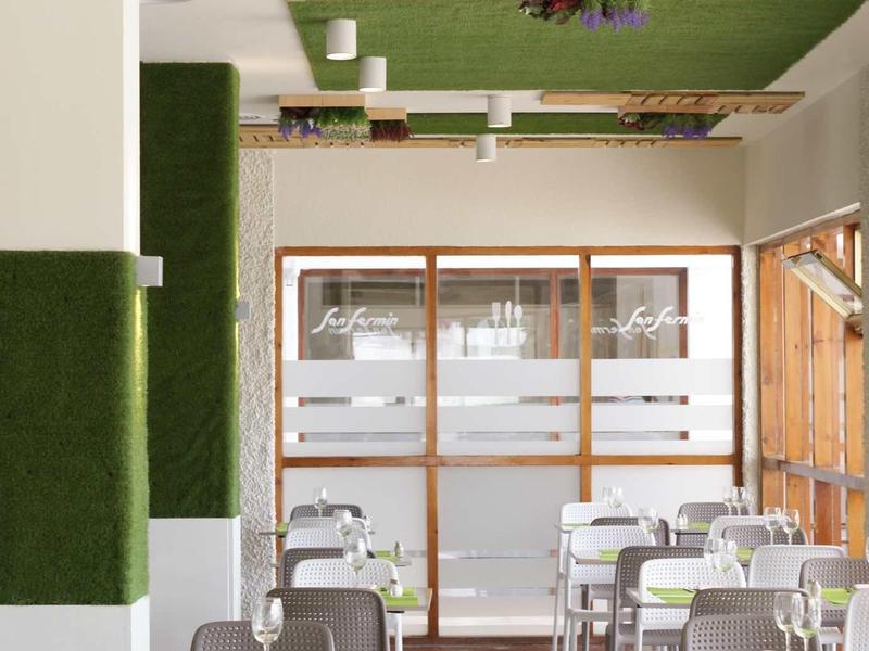 Heller, moderner Speiseraum mit grauen Stühlen, weißen Tischen und grünen Pflanzen an der Wand.