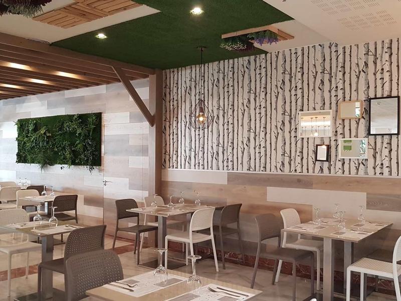 Modernes Café mit weißen Tischen, grauen Stühlen, Holzakzenten und grünem Pflanzenwand-Element.