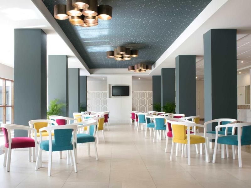 Moderner Speisesaal mit weißen Tischen, bunten Stühlen und großen Fenstern für viel Tageslicht.