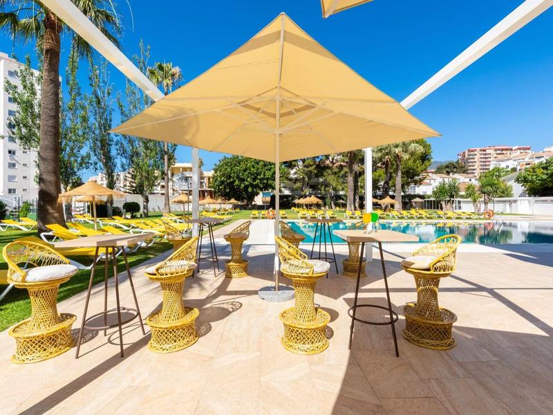 Moderner Außenbereich mit gelben Stühlen, Sonnenschirm und blauem Himmel am Pool.