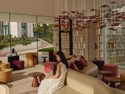 Moderne Lounge mit geschwungenem Sofa, bunter Deko und großer Glaswand im warmen Licht.