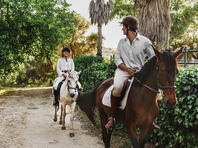 Due persone cavalcano su un sentiero stretto circondato da alberi e piante.