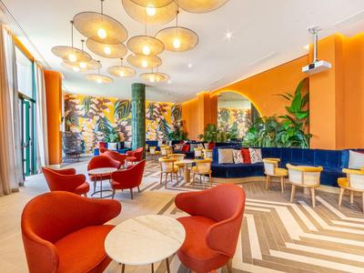 Heller, farbenfroher Raum mit orangen Wänden, roten Sesseln, blauen Sofas und Pflanzen.