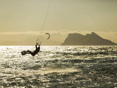 Persona che pratica kitesurf su acque mosse con isola sullo sfondo al tramonto.