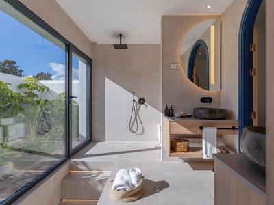 Modernes Badezimmer mit großer Glaswand, offener Dusche und rundem Spiegel an Holzmöbeln.