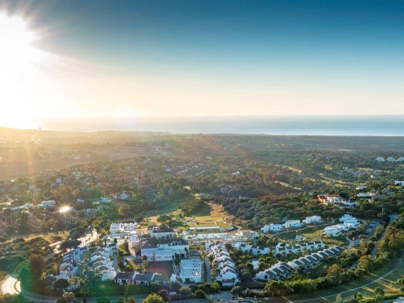 Landschaft mit Häusern, grünen Feldern und Meer am Horizont bei Sonnenaufgang oder Sonnenuntergang.
