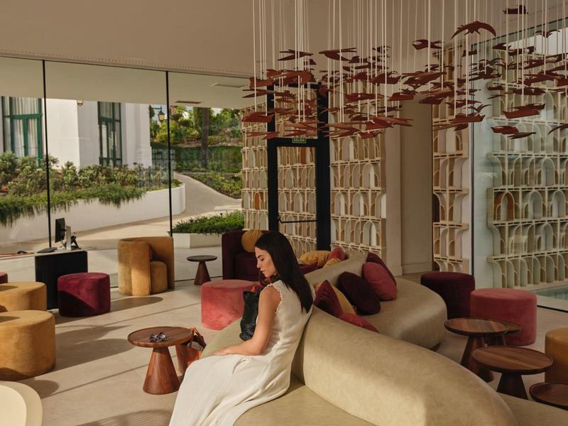 Moderne Lounge mit geschwungenem Sofa, bunter Deko und großer Glaswand im warmen Licht.