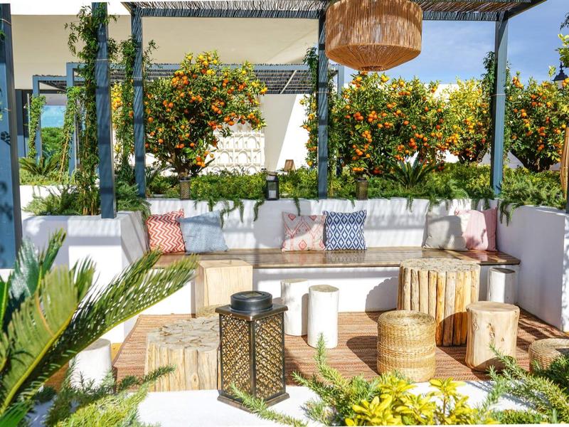 Gemütliche Terrasse mit weißen Sitzbänken, bunten Kissen, Pflanzen und Holzmöbeln unter Pergola.