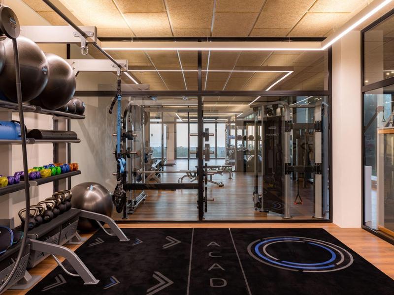 Moderner Fitnessraum mit Hanteln, Bänken, Spiegeln und Holzdecke in neutralen Farben.