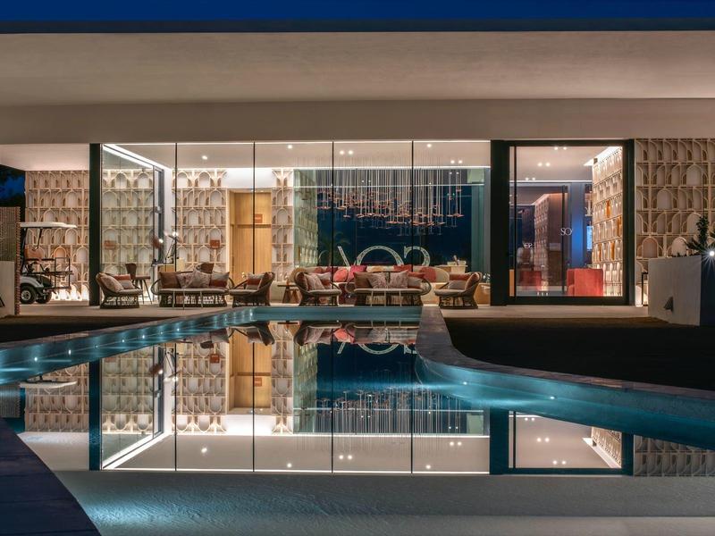 Moderner Wohnraum mit großem Schwimmbecken, Glasfronten und warmem Innenlicht bei Nacht.