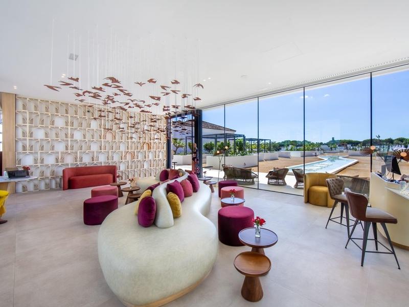 Moderner Wohnraum mit großen Glasfronten, bunter Sitzgruppe und dekorativen Elementen an der Decke.