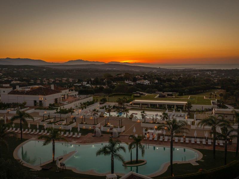 Sonnenuntergang über Hotelanlage mit Pool, Palmen und umliegender Stadtlandschaft.