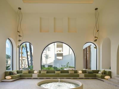 Großer Raum mit runden Fenstern, langem grünen Sofa und rundem Tisch in der Mitte unter hohen Decken.