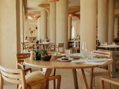 Moderner Gastraum mit runden Holztischen, Stühlen und Säulen in warmen Beige- und Brauntönen.