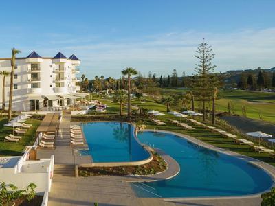 Hotel con una gran piscina exterior curva y tumbonas bajo un cielo despejado