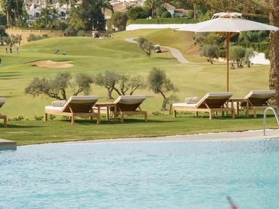 Schwimmbecken mit blauer Wasserfläche, Liegestühlen auf grünem Rasen und Sonnenschirm im Hintergrund.