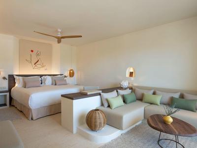 Modernes Schlafzimmer mit großem Bett, gemütlicher Sitzecke und neutralen Farben, hell und minimalistisch.