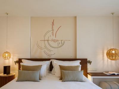 Schlafzimmer mit Doppelbett, hellen Wänden, abstrakter Wandkunst und runden Holzlampen neben dem Bett.